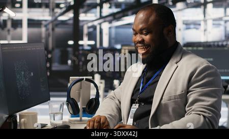 Cheerful data center worker dancing from joy after finishing supercomputers system maintenance. Happy engineer overjoyed by successful AI model training results, overseeing server equipment, camera A Stock Photo