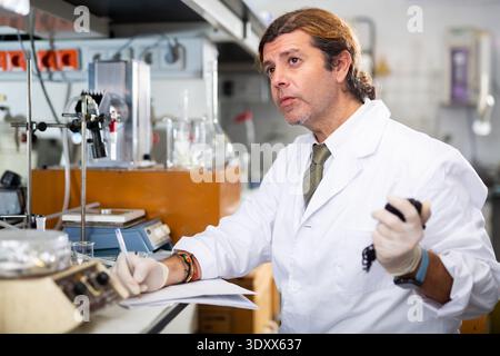 Scientist Latin man writing down result report on paper while analyzing experiment in laboratory Stock Photo