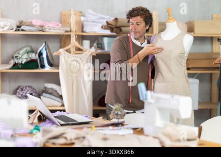 Man seamstress communicates with customer via video call using laptop, work with mannequin Stock Photo