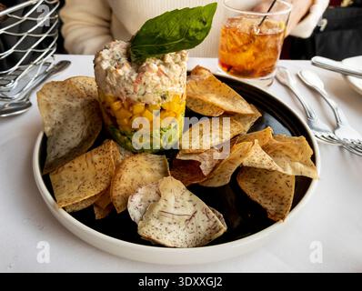 A layered seafood salad with creamy shrimp topping, diced mango, and fresh avocado, garnished with basil and served with crisp house-made chips for a Stock Photo