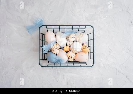 Easter eggs in metal wire basket with blue feathers on gray textured background. Top view, flat lay Stock Photo