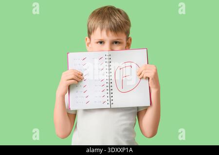 Sad schoolboy holding notebook with bad results of school test on green background Stock Photo