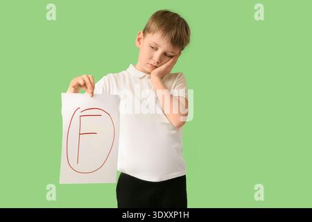 Sad schoolboy holding paper with bad grade on green background Stock Photo