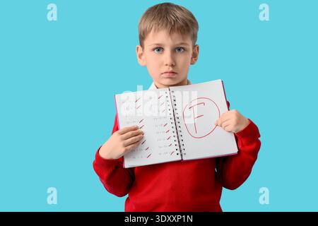Sad schoolboy holding notebook with results of school test on blue background Stock Photo
