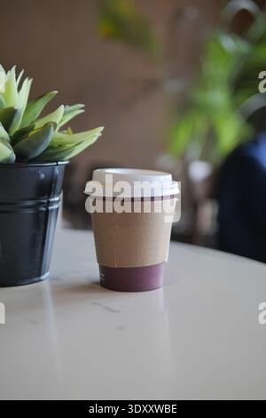 Coffee cup on table next to a plant in a cafe Stock Photo
