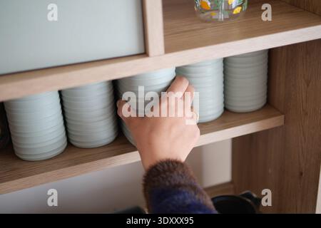 Hand reaches for ceramic dishes on a wooden shelf Stock Photo