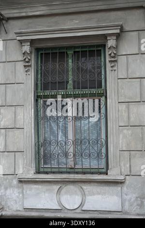 a vintage window with a green-trimmed wooden frame protected by an ornate wrought iron grille. Stock Photo