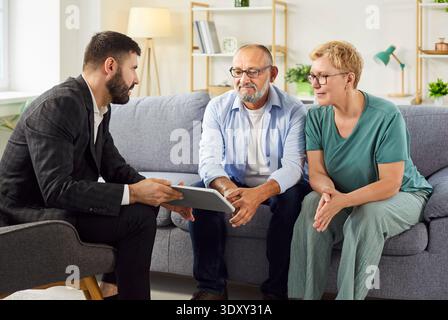 Real estate agent explaining terms to mature couple using tablet in living room Stock Photo