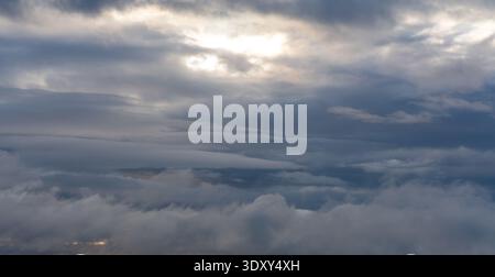 Layers of heavy grey clouds fill the sky with light breaking through a central opening creating airy and atmospheric feeling Stock Photo