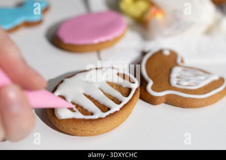 A person decorates various gingerbread cookies for Easter. The scene shows colorful icing and different shapes, such as bunnies and eggs, on a white table. This activity is part of a family tradition. Stock Photo