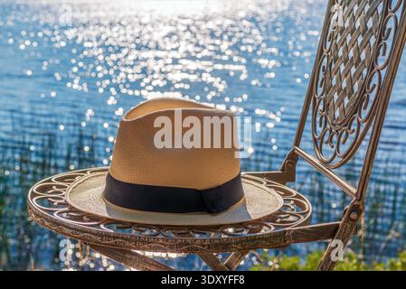 A panama hat on a chair by a lake Stock Photo