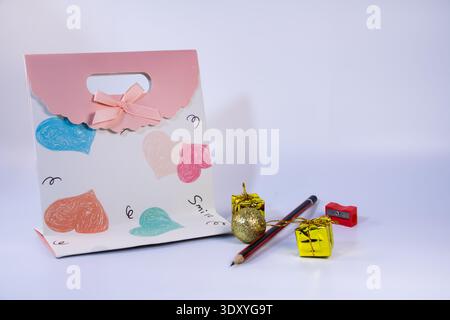 Decorative gift bag with heart patterns, pencil, sharpener and small golden gift boxes isolated on white background. Still life concept for celebratio Stock Photo