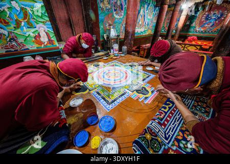 Several monks in traditional robes and face masks carefully assemble a complex sand mandala on a flat surface within the Hemis Gompa. Leh district Uni Stock Photo