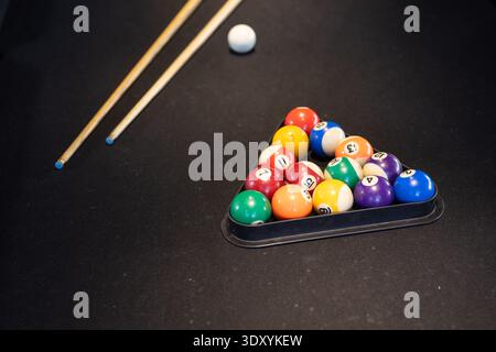 Triangular rack holding 15 glossy numbered balls on dark felt, cues lying diagonally, copy space Stock Photo