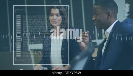 Discussing two professionals analyzing data in meeting room, in suits, laptop with digital overlays Stock Photo