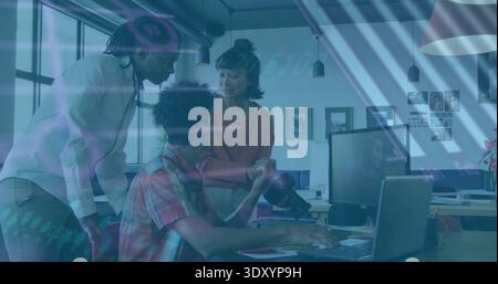 Editing photographer in checked shirt using DSLR, laptop in office, colleague leaning in peach knit Stock Photo