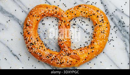 Freshly baked homemade Pretzel with black and white sesame seeds on a marble background. Traditional savory pastries. German (Bavarian) beer appetizer Stock Photo