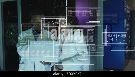 Analyzing two engineers wearing white lab coats examining hologram data in server room, with tablet Stock Photo