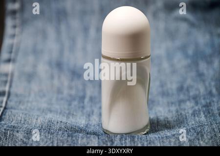 A small glass bottle of deodorant on a blue jeans denim background Stock Photo