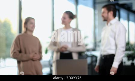 Three people are standing in a room, one of them is holding a laptop Stock Photo