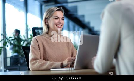 A woman is sitting at a desk with a laptop in front of her Stock Photo