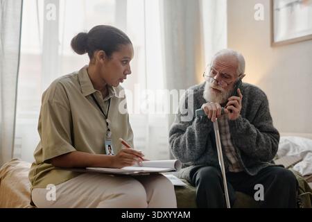 Young Adult Black Woman Social Worker Assisting Senior Caucasian Man Talking Stock Photo