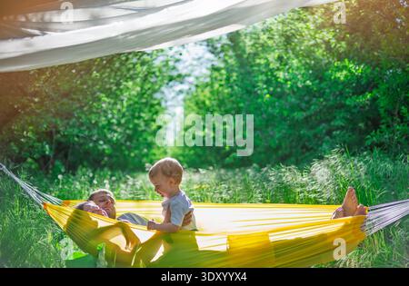 Family relaxing in yellow hammock in sunny green nature Stock Photo
