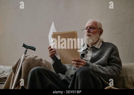 Senior Caucasian Man Reading Documents While Sitting Beside Walking Cane Stock Photo
