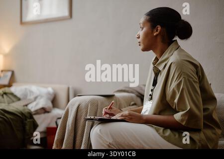 Young Adult Black Woman Social Worker Taking Notes during Home Visit Stock Photo