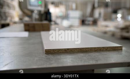 White laminated chipboard panel on a worktable in a furniture manufacturing workshop with blurred background. Stock Photo