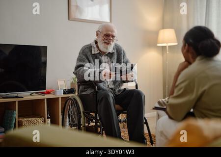 Senior Caucasian Man in Wheelchair Holding Brochure with Social Worker Indoors Stock Photo