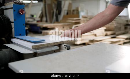 Worker processing a laminated particle board panel on industrial machinery in a furniture workshop. Stock Photo