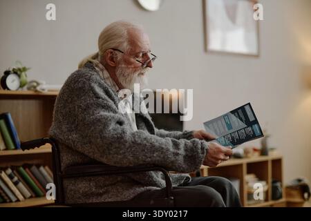 Senior Caucasian Man in Wheelchair Reading Documents during Social Work Visit Stock Photo