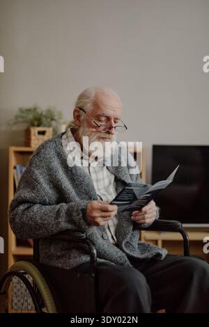 Senior Caucasian Man with Disability Reading Document in Living Room Stock Photo