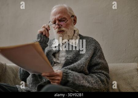 Senior Caucasian Man Reading Documents While Sitting Indoors on Sofa Stock Photo