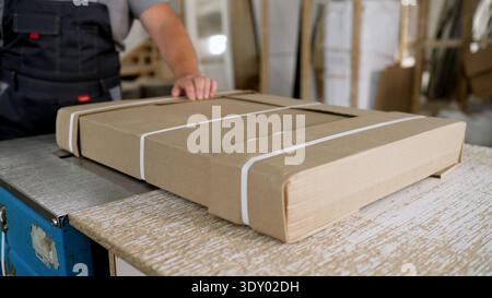 Worker in overalls packing a cardboard box with furniture parts in a factory. Stock Photo