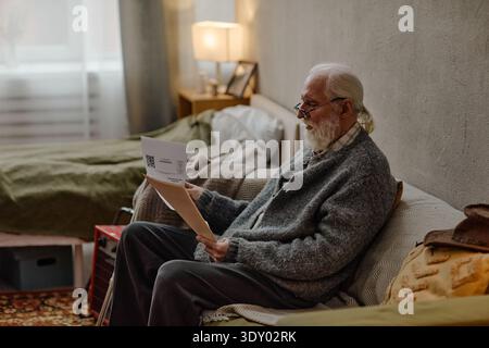Senior Caucasian Man Sitting Indoors Checking Bills with Focused Expression Stock Photo