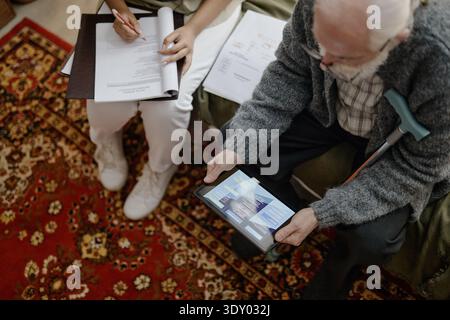 Senior Caucasian Man Consulting Social Worker Using Digital Tablet Indoors Stock Photo