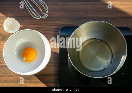 Top view of separated egg components with yolk in a white bowl and egg white in a metal bowl on kitchen scales. Stock Photo