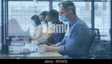 Typing mature man at right in denim shirt using laptop at office, masked coworkers, charts, tablet Stock Photo