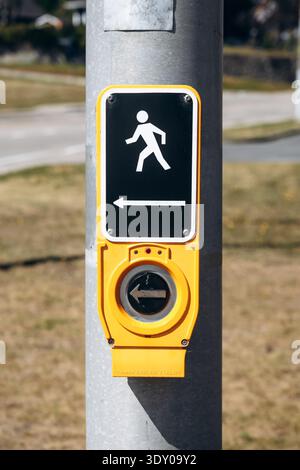 La Malbaie, Canada - August 22, 2025: Pedestrian crossing push button with walking symbol and directional arrow mounted on a traffic signal pole at a Stock Photo