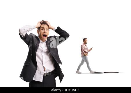 Shocked businessman in a torn suit looking at a distracted man walking into a hole while looking at his phone Stock Photo