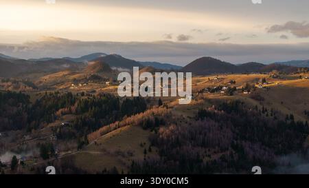 Aerial view of golden sunlight kissing the rolling hills and scattered houses, painting a serene landscape in warm hues, Șirnea, Brașov, Romania. Stock Photo