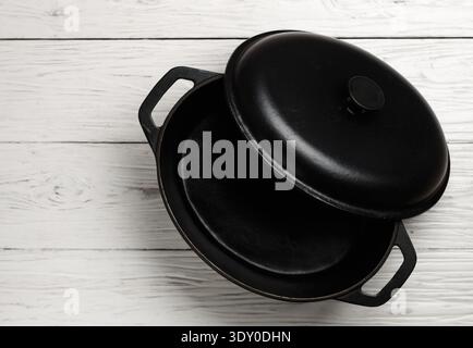 Cast iron pot with lid. A casserole pot On a on a white wooden background. Empty clean Castiron cooking utensils. Top view, copy space Stock Photo