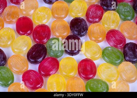 Multicolored hard candies scattered on white surface, glossy sugar crystals catching light, vibrant red yellow green purple pieces, playful party vibe Stock Photo