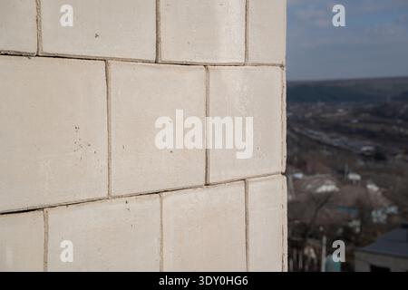 Corner of multi storey residential building facade covered with white cladding panels with blurred urban landscape and hills in background. Stock Photo