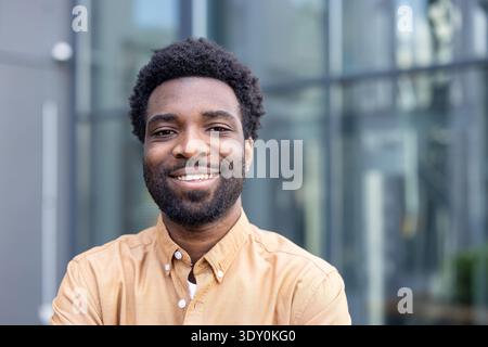 Young businessman with afro hairstyle smiling confidently outdoors in an urban setting, smart-casual and approachable, portrait conveying success, leadership and a bright future Stock Photo