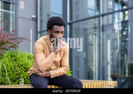 Young man sitting outdoors reflecting on life challenges, experiencing anxiety and feeling sad and worried while contemplating difficult decisions or a stressful situation Stock Photo