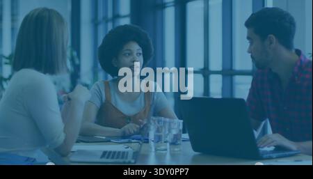 Leading woman speaking in modern meeting room, wearing gray tee under brown dress, with two laptops. Leadership, collaboration, discussion, planning, Stock Photo