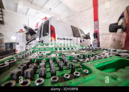Low angle close-up of a green socket set on a workbench, with a white service van being repaired in a workshop. Stock Photo